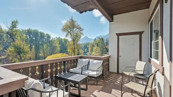 Un balcon avec des meubles d’extérieur, une vue sur les arbres et les montagnes, et une porte.