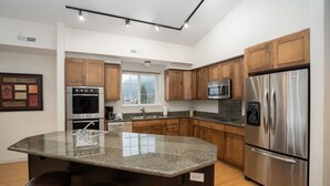 A modern kitchen with granite countertops, stainless steel appliances, wooden cabinets, and a large island with bar stools. - Obertal Inn (Leavenworth)
