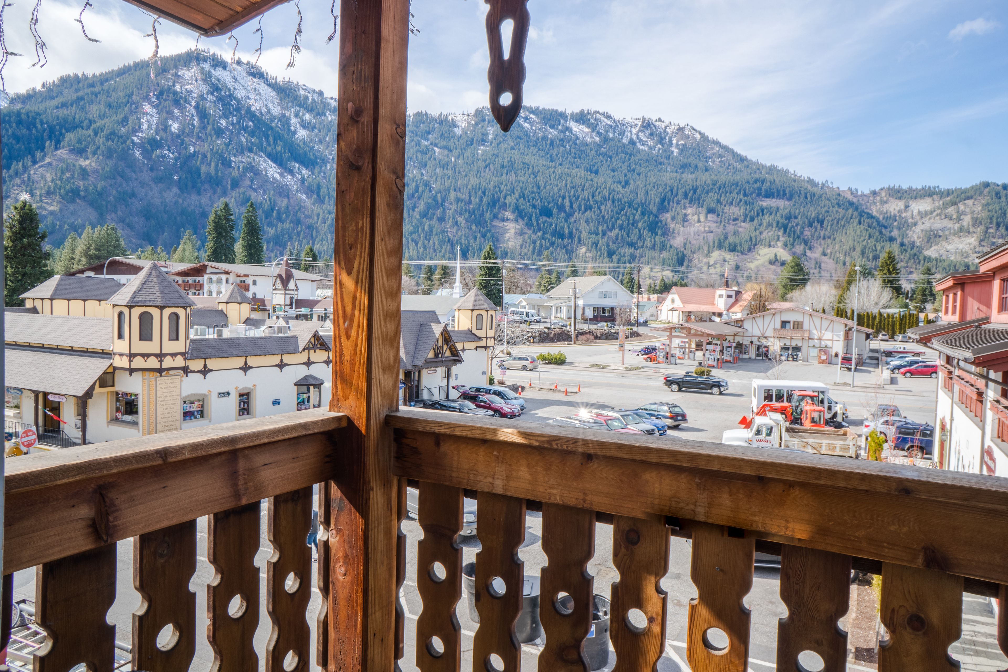 A mountain town with a view of snow-capped mountains, a street with cars, and buildings with traditional architecture.