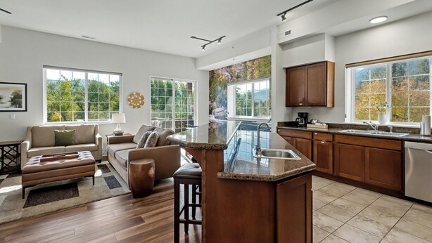 A modern kitchen with a central island, wooden cabinets, and large windows offering views of trees. - Obertal Inn (Leavenworth)