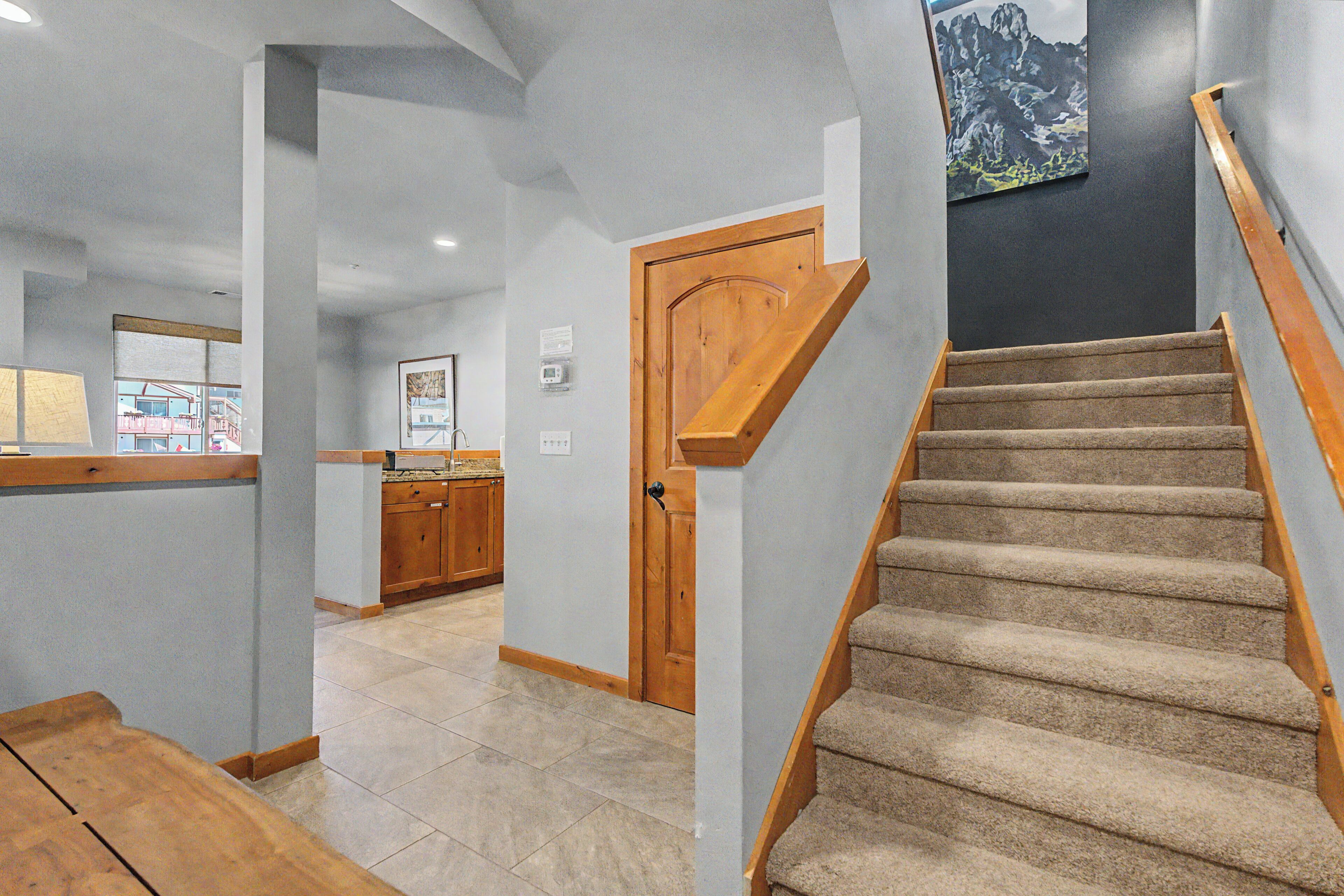 A staircase with carpeted steps, a wooden handrail, and a door leading to a kitchen area.