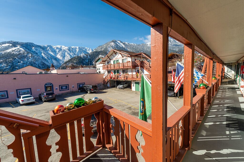 A hotel balcony with a view of snow-covered mountains, a parking area with cars, and a flag display.