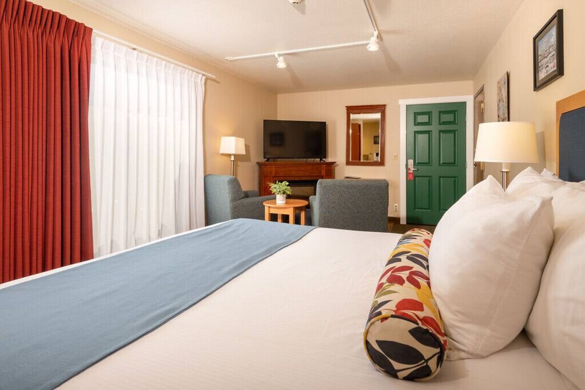 Una habitación de hotel con una cama, televisión, una puerta verde y una mesita con lámpara.