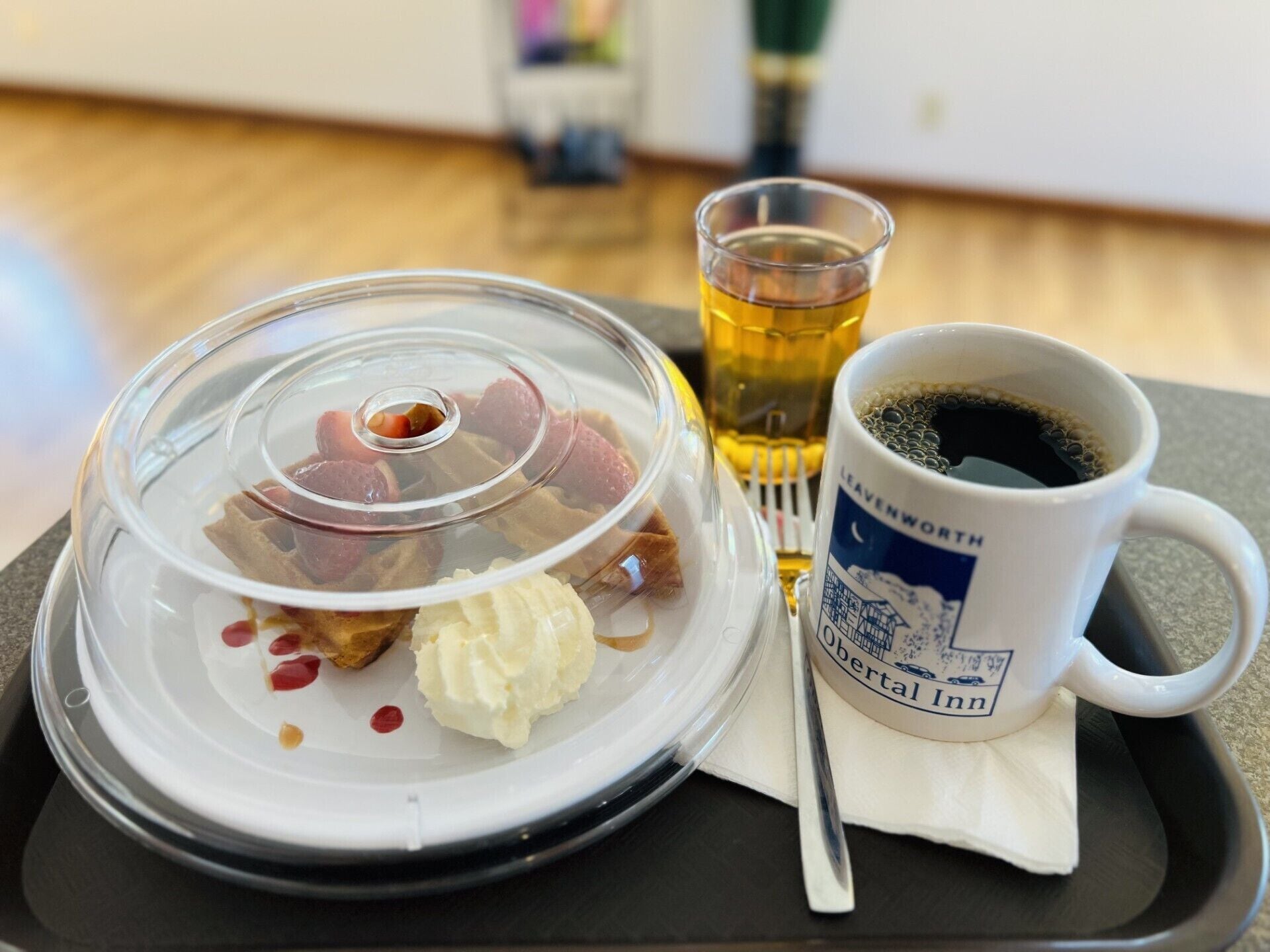 Un repas composé d’un plat couvert, d’un verre contenant un liquide ambré et d’une tasse blanche avec du texte.