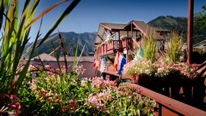 A traditional chalet with a balcony, surrounded by lush greenery and flags. - Obertal Inn (Leavenworth)