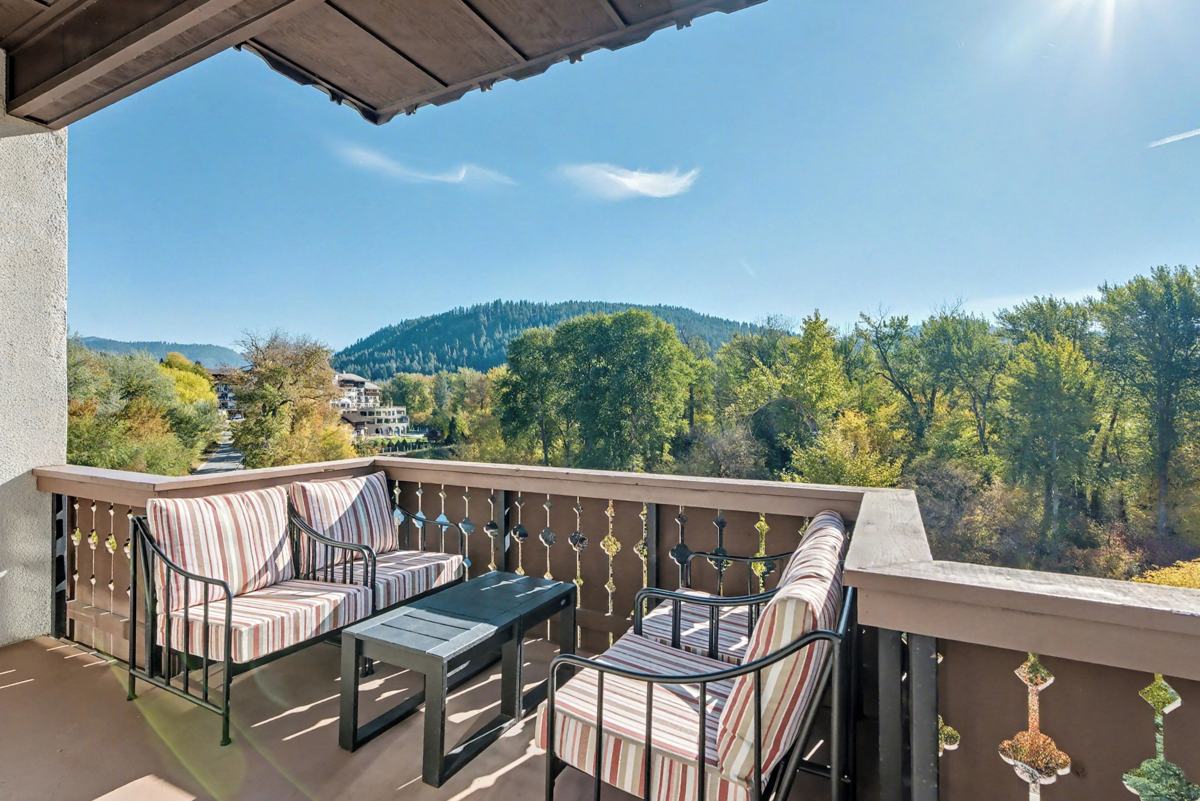 A balcony with a sofa and table, offering a view of a forested hillside.