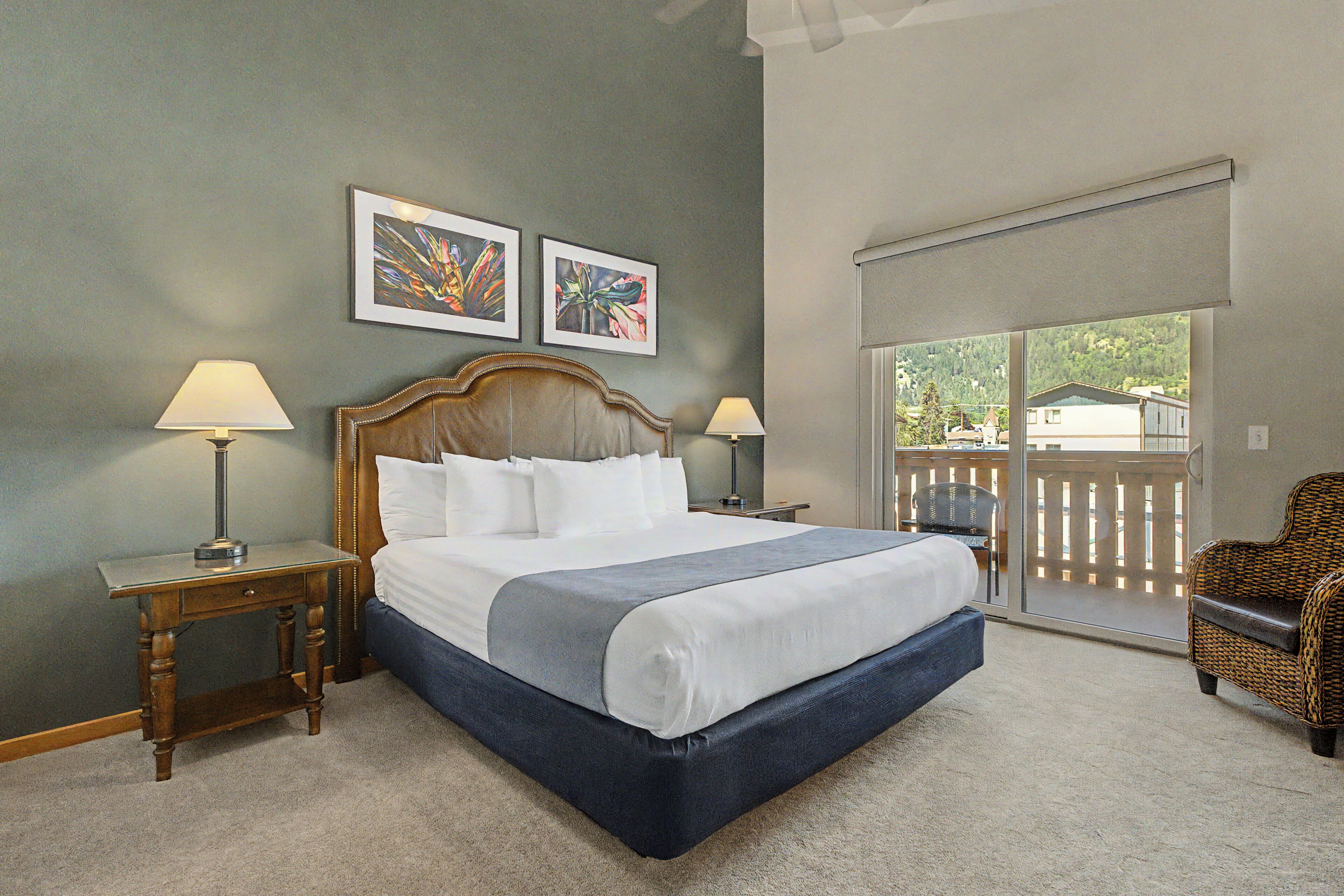 A bedroom with a large bed, two bedside tables with lamps, a chair, and a balcony with a view.