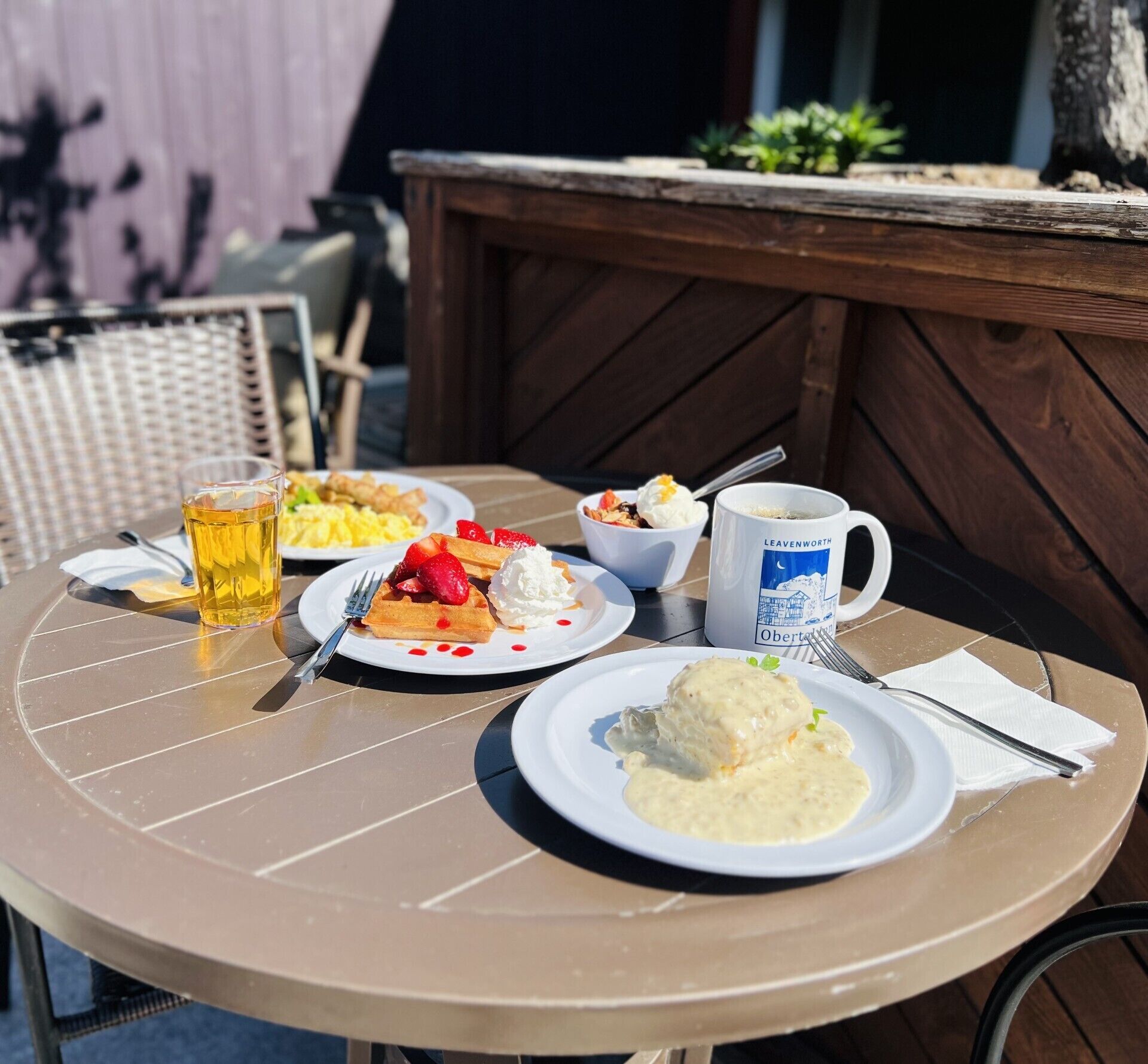 A round outdoor table with plates of food, a mug, and a glass of beer.