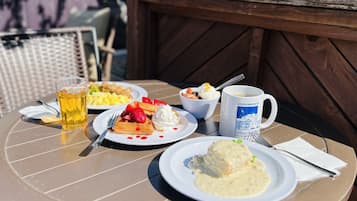 Una mesa redonda al aire libre con platos de comida, una taza y una jarra de cerveza.