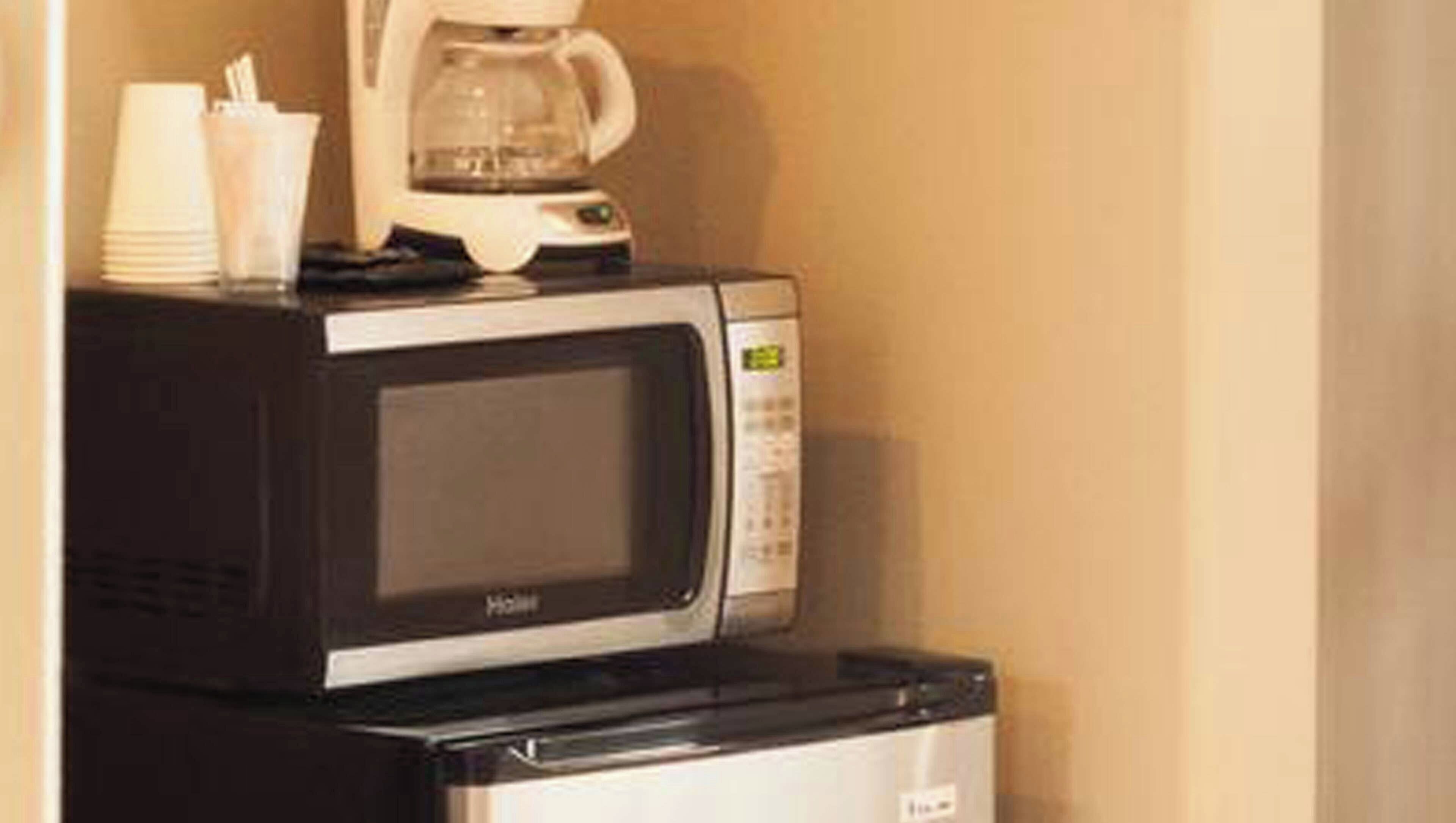 A microwave and coffee maker on a countertop, with a stack of white plates and a glass of water nearby.