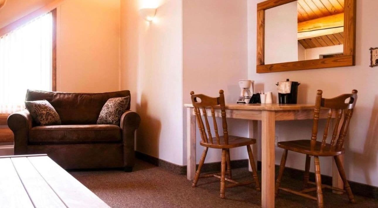 Una habitación con un sofá de cuero marrón, dos sillas de madera, una mesa de madera y un espejo en la pared.
