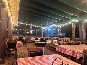 An outdoor restaurant with wooden tables and benches, string lights, and a view of the night sky. - Dodge Peak Lodge (Bonners Ferry)
