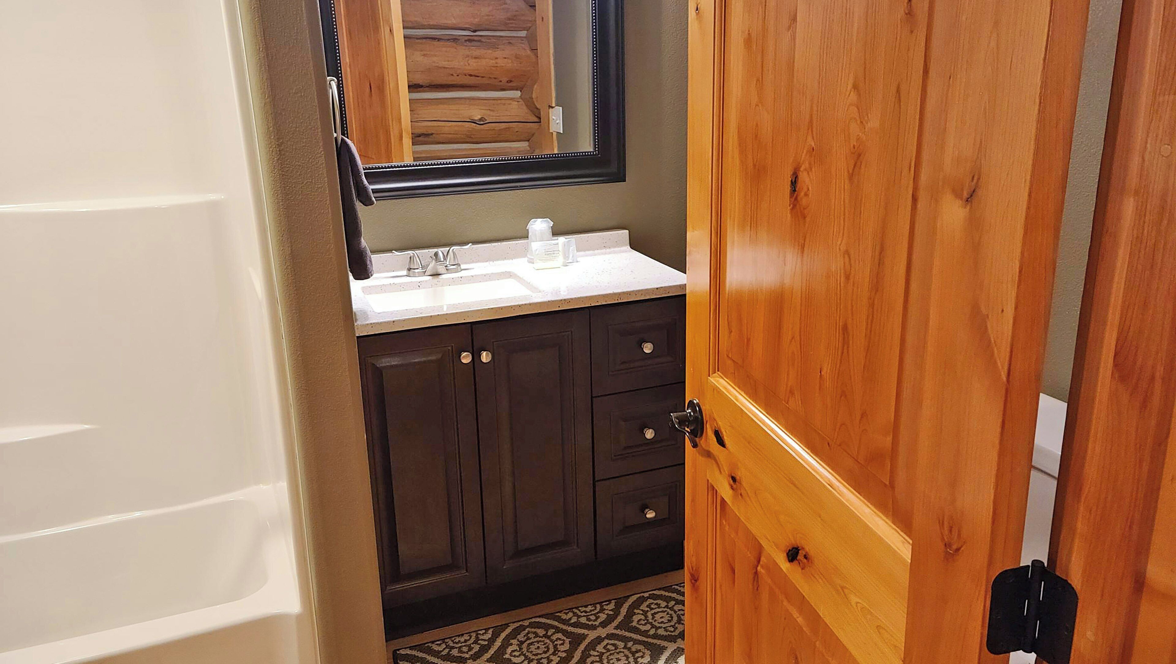 A bathroom with a wooden door, dark cabinets, a white sink, and a mirror.