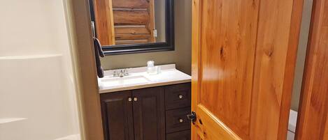 A bathroom with a wooden door, dark cabinets, a white sink, and a mirror.