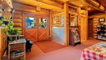 A log cabin interior with wooden walls, a reception desk, a check-in counter, and a bed with a checkered bedspread.