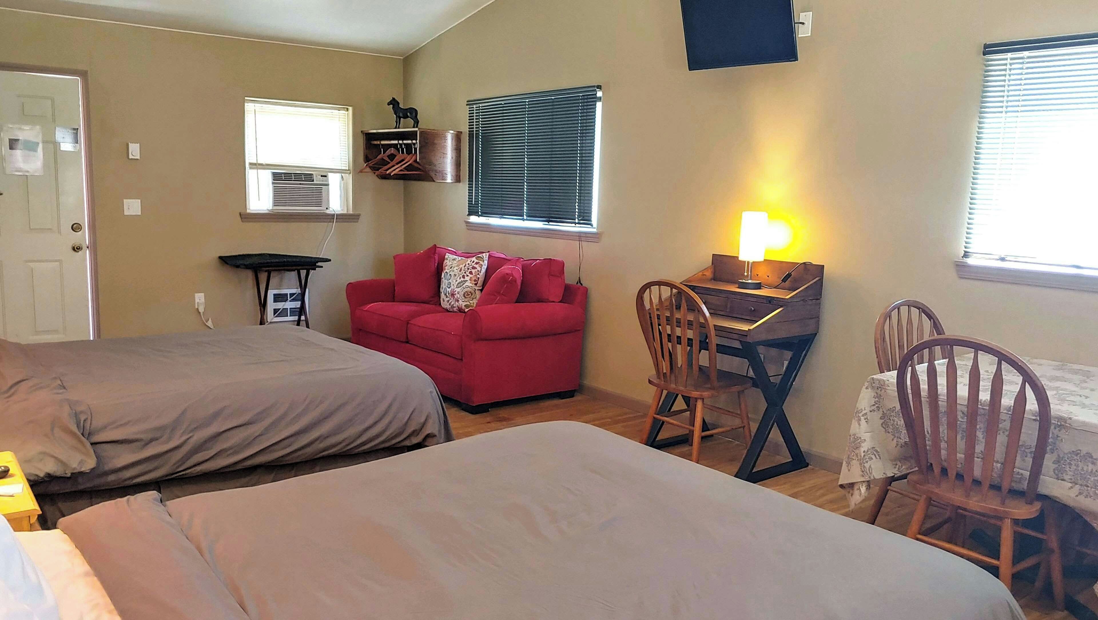 Ein Schlafzimmer mit zwei Betten, einem roten Sofa, einem Schreibtisch mit Lampe und einem Sessel.