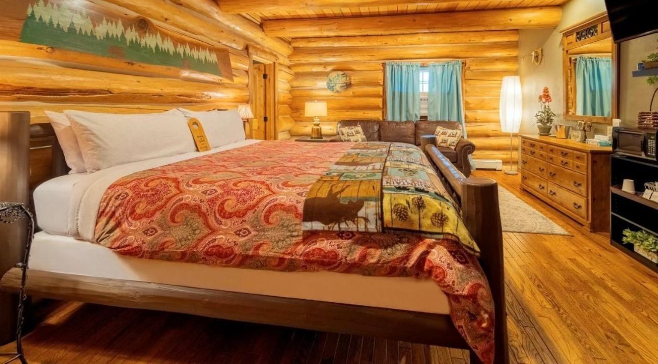 A log cabin-style bedroom with a large bed, a dresser, a nightstand, and a painting on the wall.