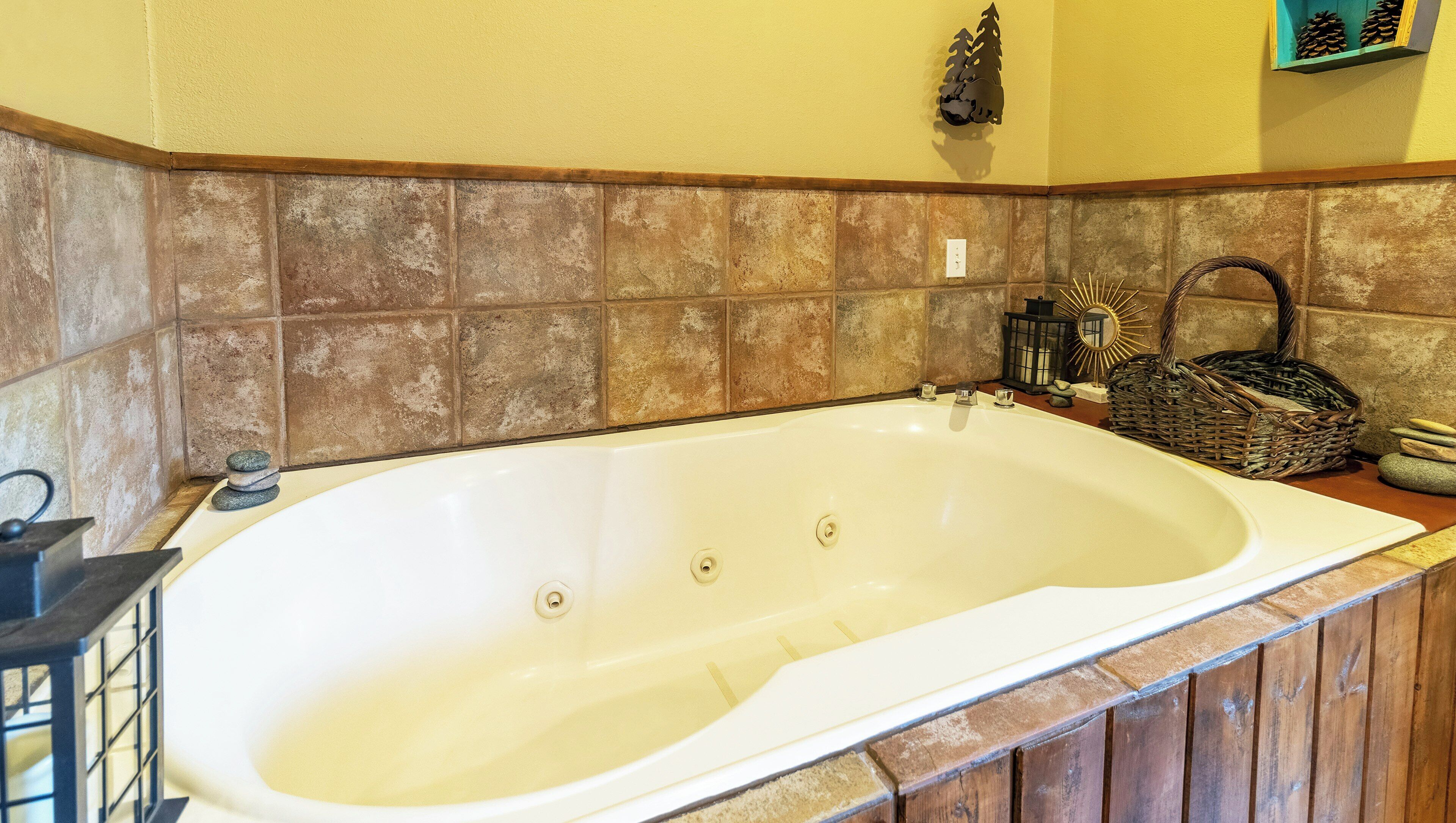 A bathroom with a large bathtub, stone tiles, a wooden bench, and a decorative wall piece.