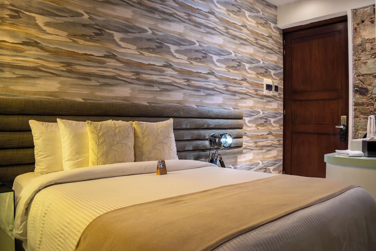 Un dormitorio con cabecera de piedra, una puerta de madera y una mesita de noche con lámpara.