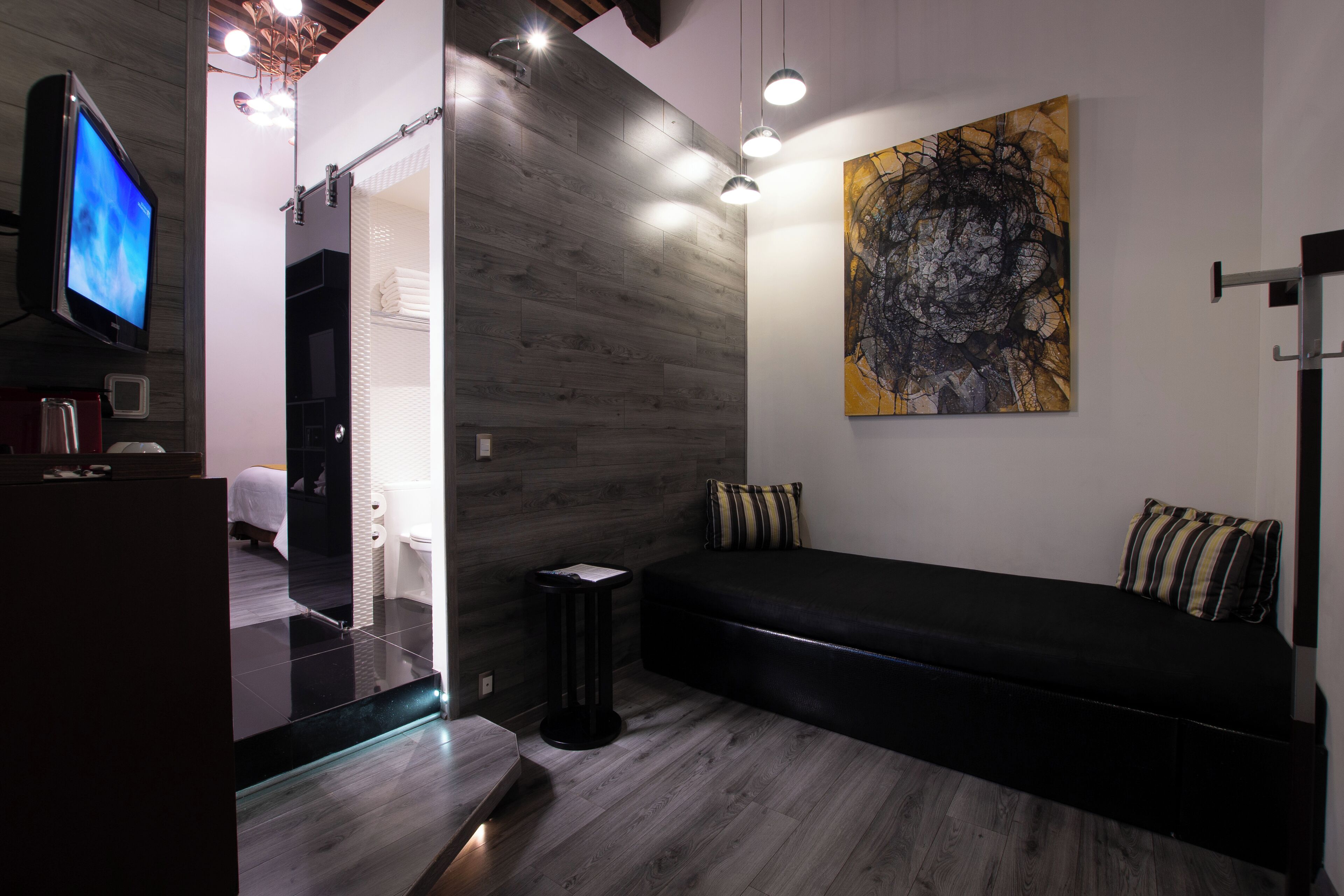 A modern bathroom with a wooden floor, a black bench, and a large abstract painting on the wall.