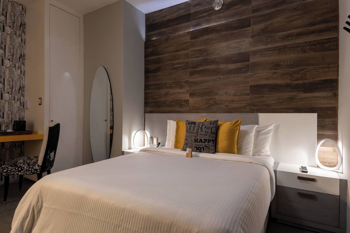 Un dormitorio ordenado con una cama grande, mesitas de noche, un escritorio y una silla.