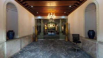 A marble-floored lobby with a chandelier, a reception desk, and a chair.