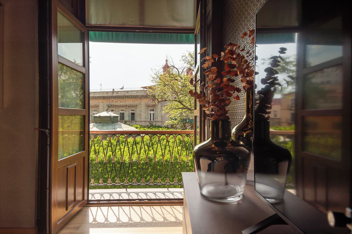 Una ventana abierta con vistas a un edificio y un balcón con barandilla.