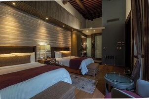 Una habitación de hotel moderna con dos camas, una zona de estar y una mesa de vidrio.