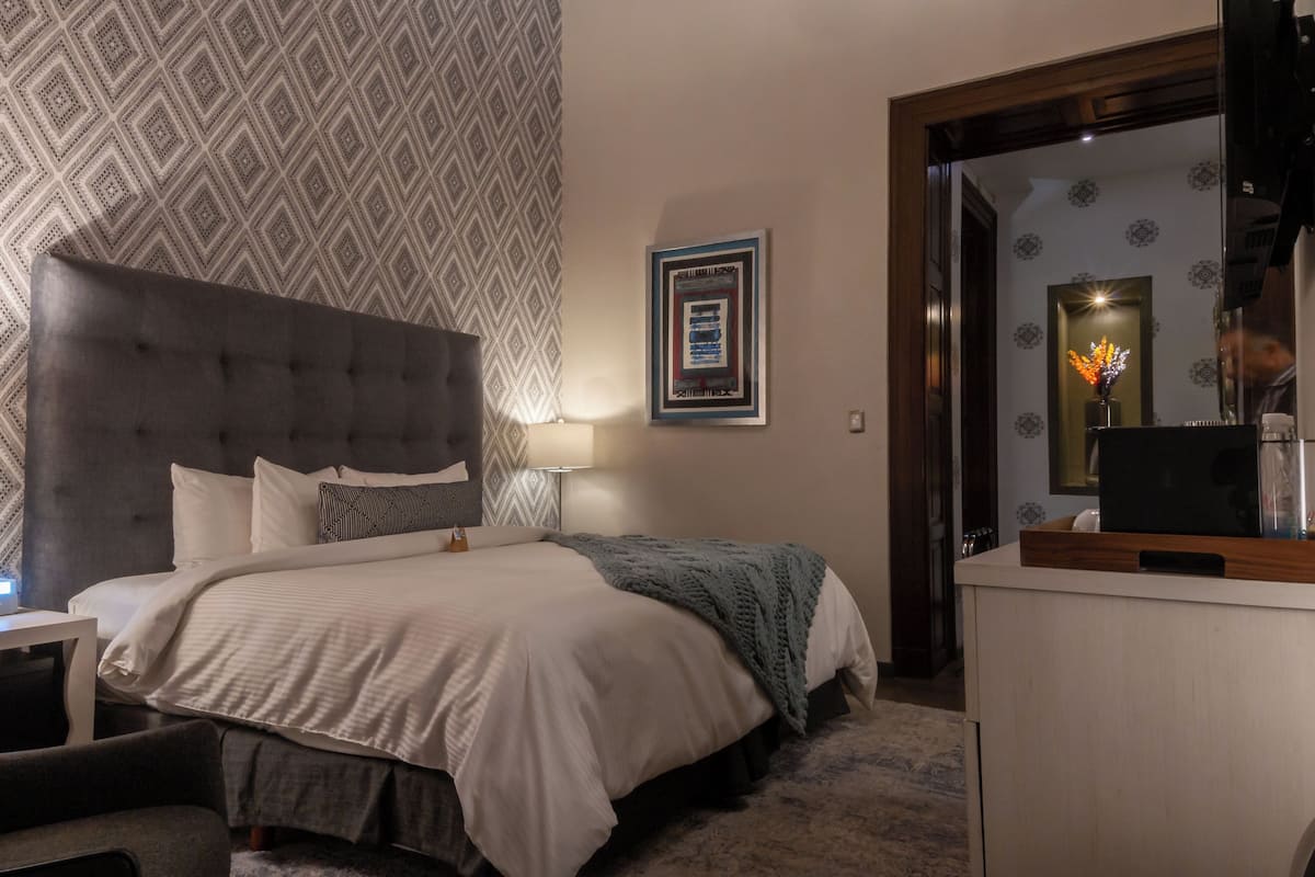 Un dormitorio ordenado con una cama grande, una mesita de noche, una lámpara y un espejo.