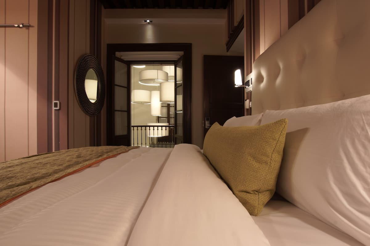 Una habitación de hotel con una cama, un espejo y un pasillo que lleva a un baño con puerta de cristal.