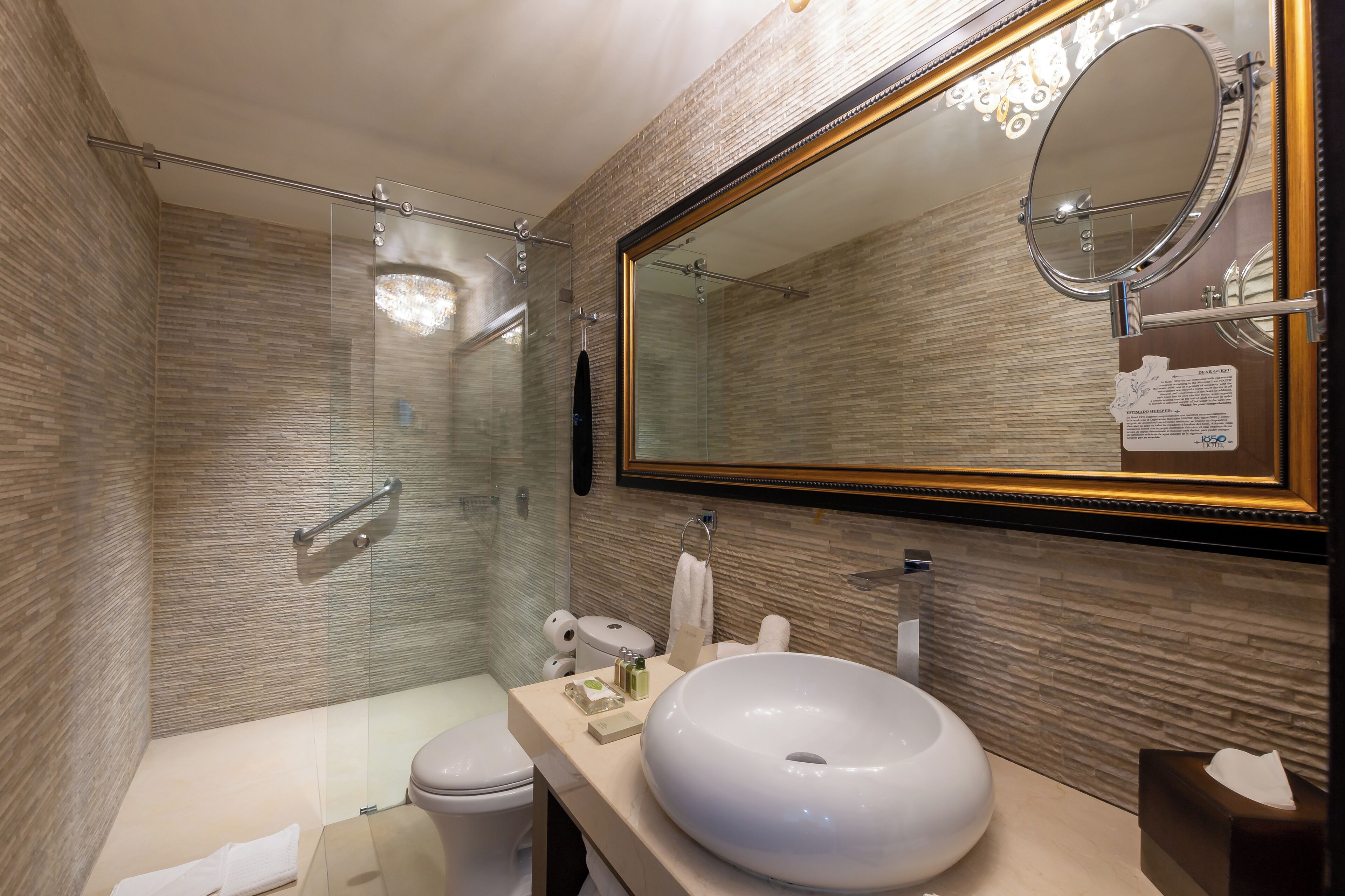 A modern bathroom with a large mirror, a round sink, and a glass-enclosed shower.