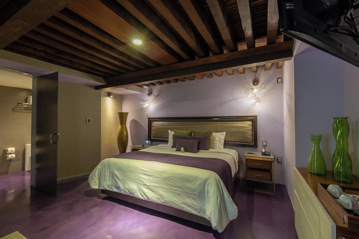 Un dormitorio moderno con una cama grande, vigas de madera en el techo, una mesita de noche y jarrones decorativos.