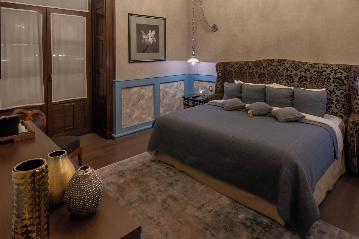 Un dormitorio con una cama grande, una araña, techo de madera y una mesita de noche con objetos decorativos.