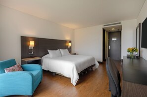 Une chambre d’hôtel équipée d’un lit, d’un bureau, d’une chaise, d’une table de chevet et d’une lampe fixée au mur.