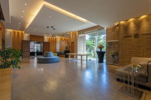 A modern hotel lobby with a seating area, a reception desk, and a large window offering a view of the outdoors.