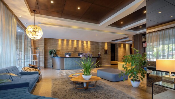 A modern hotel lobby with a reception desk, sofas, a coffee table, and potted plants.