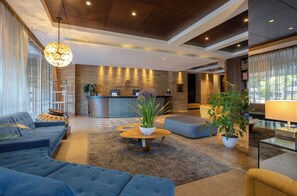 Un hall d’hôtel moderne avec un comptoir d’accueil, des canapés, une table basse et des plantes en pot.