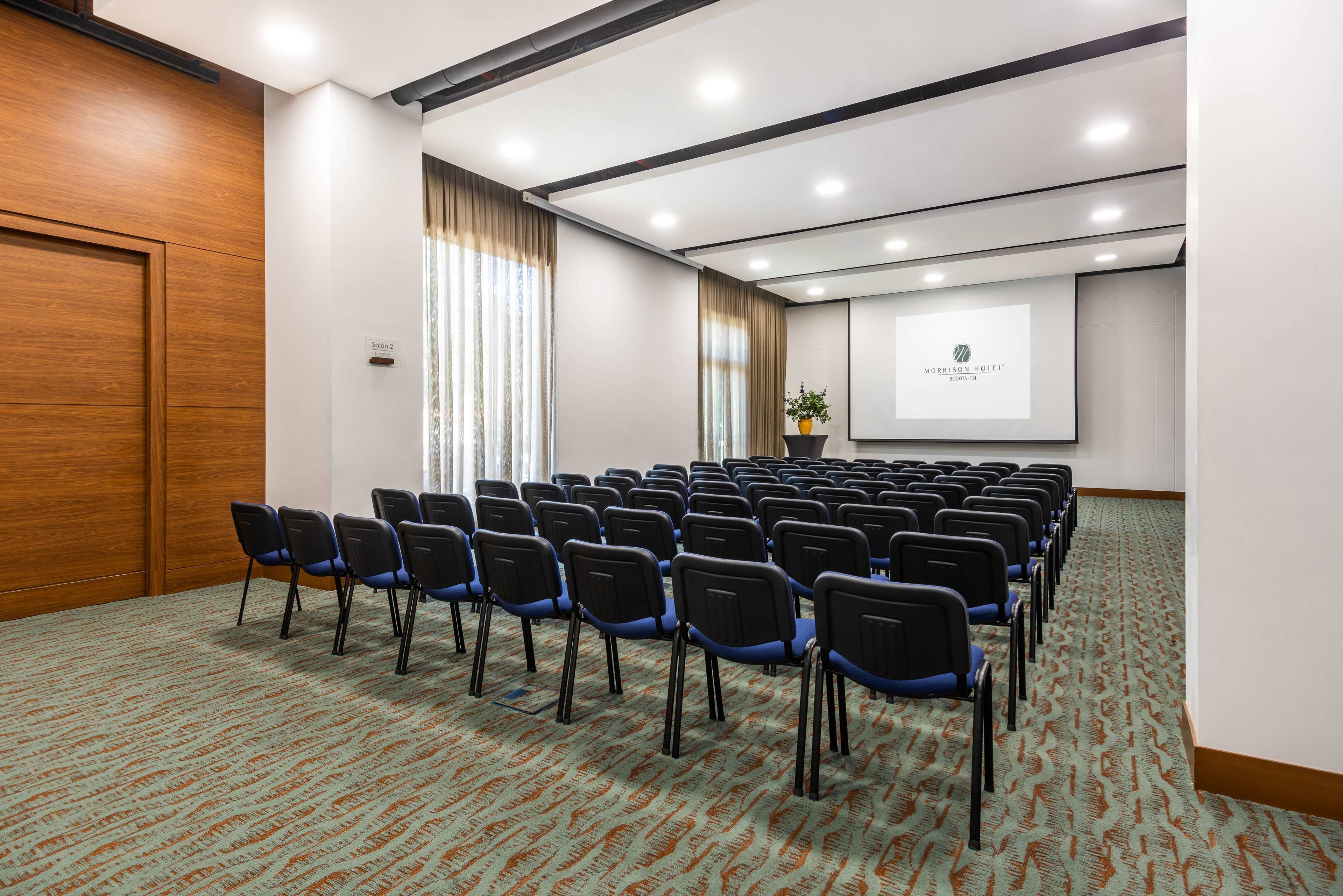 A conference room with rows of chairs, a projector screen, and a wooden door.