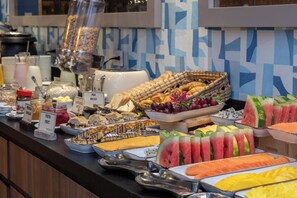 Un buffet proposant une variété de plats, notamment des fruits, des sandwichs et des pâtisseries.