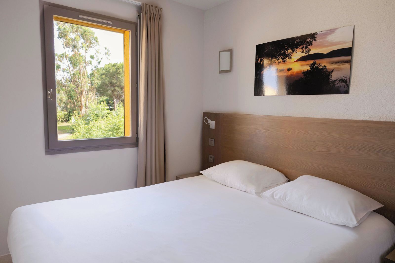 A hotel room with a bed, a window with curtains, and a painting on the wall.