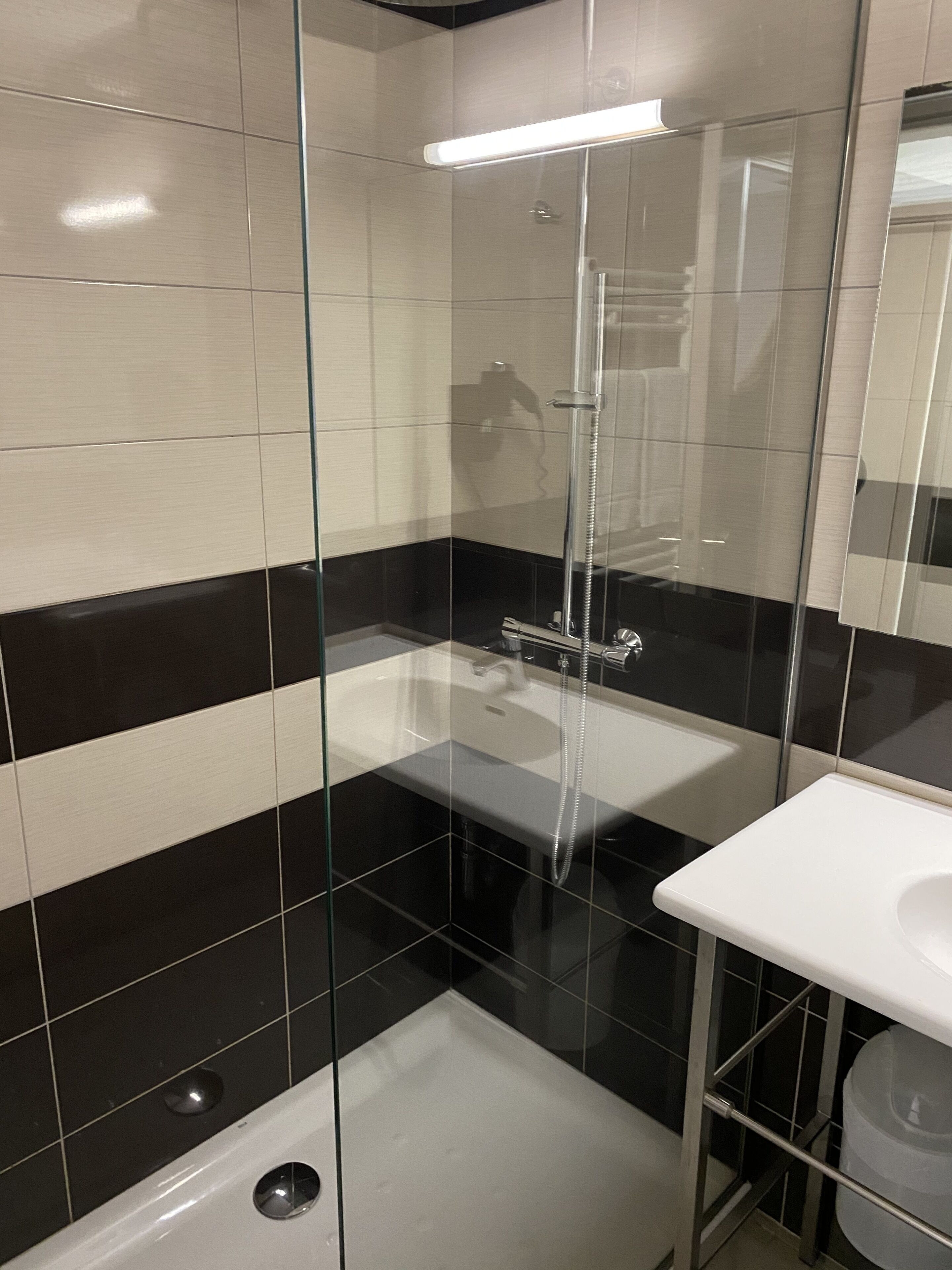 A modern bathroom with a glass-enclosed shower, a white sink, and black and white tiled walls.