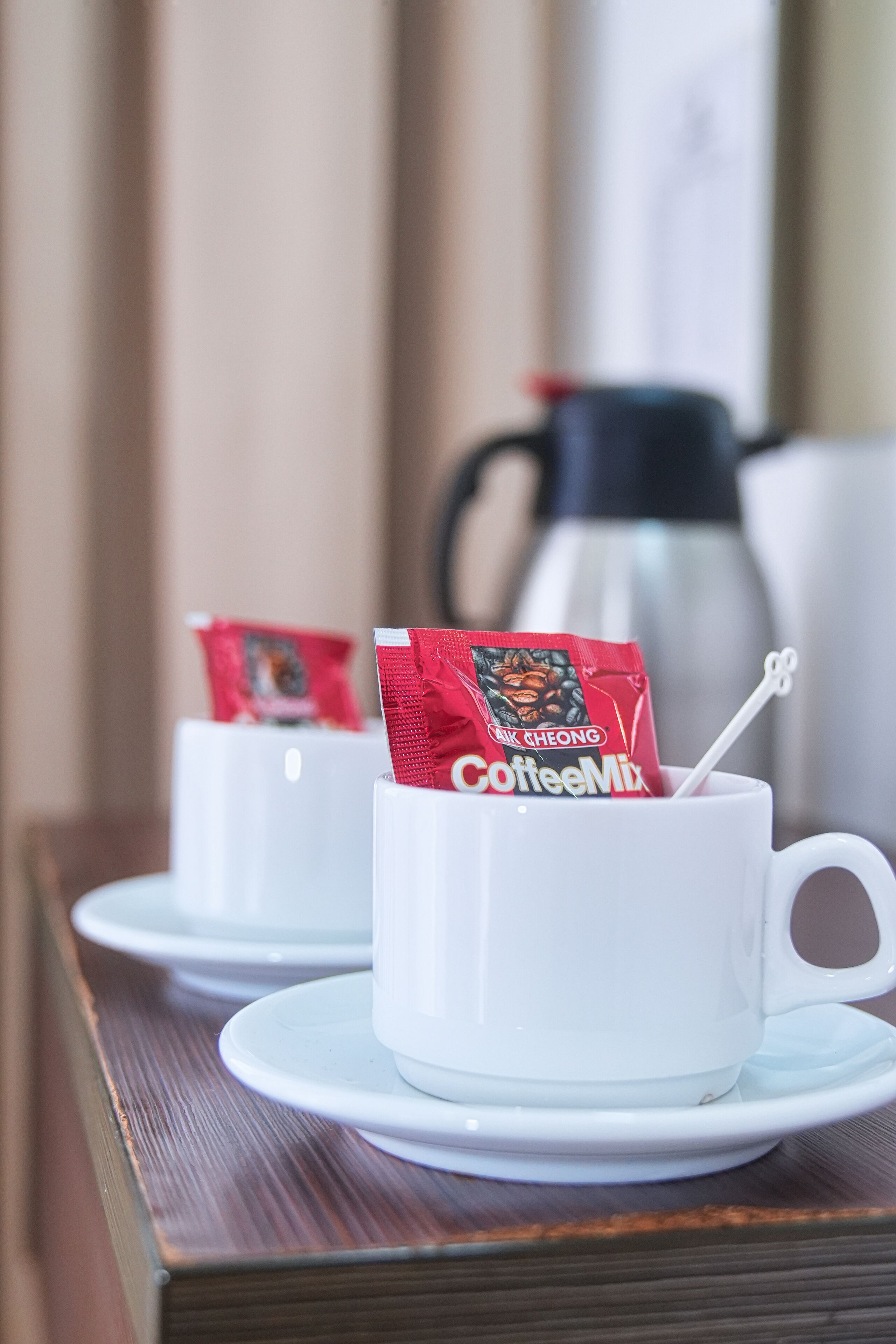 Deux tasses blanches accompagnées de sachets de café posés sur des soucoupes, une cafetière blanche et une table en bois.
