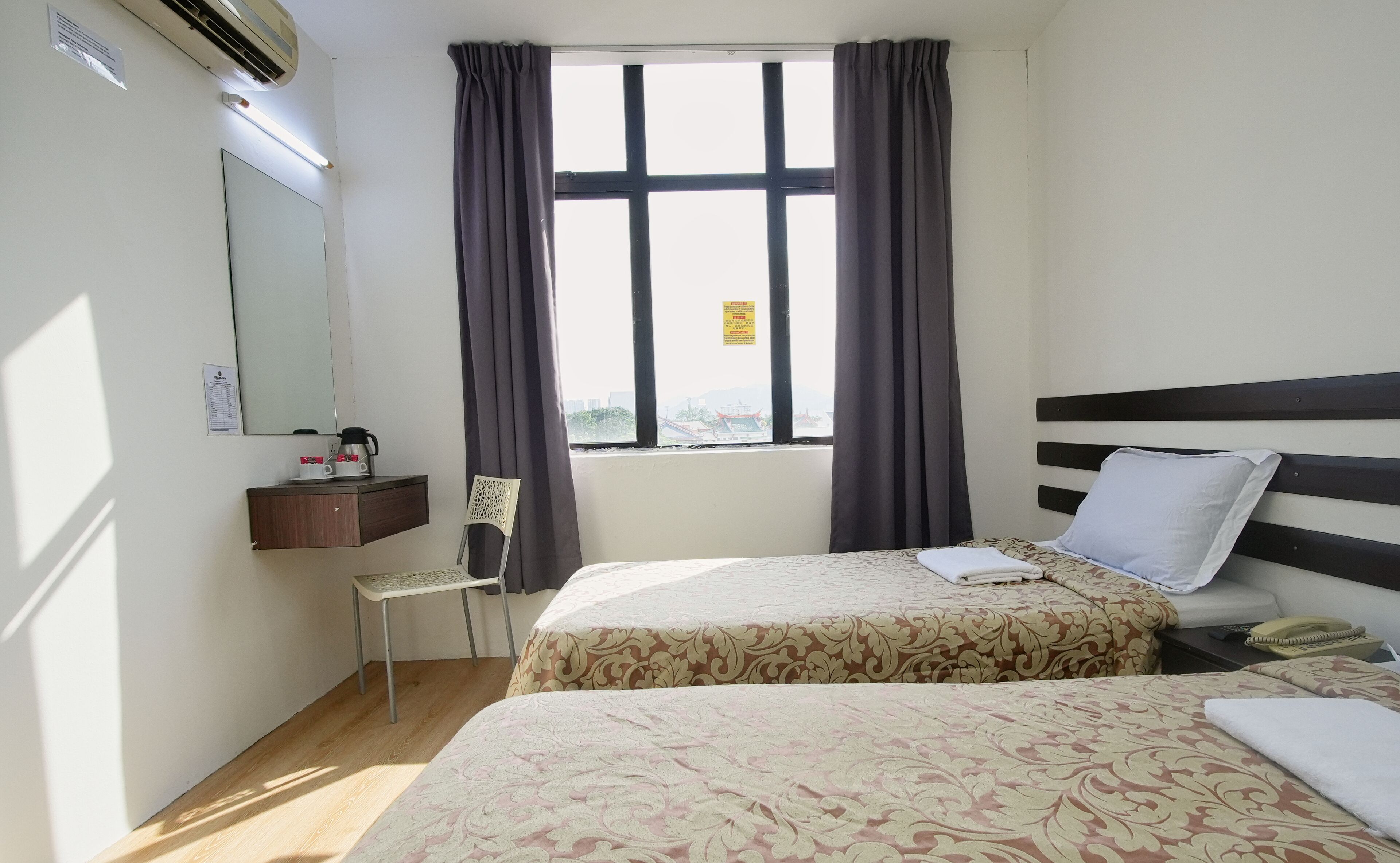 A hotel room with two beds, a desk with a chair, a mirror, and a window with curtains.