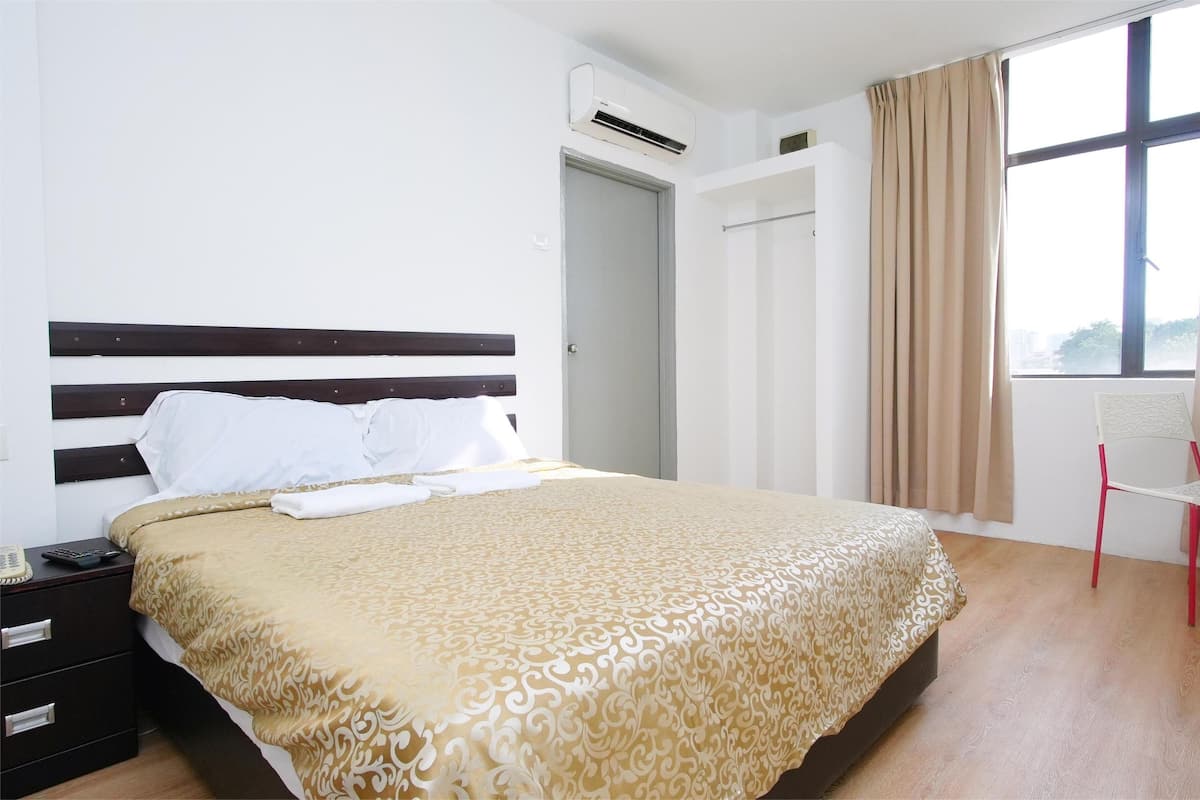 Una habitación de hotel ordenada con una cama grande, una mesita de noche, una silla y una ventana con cortinas.
