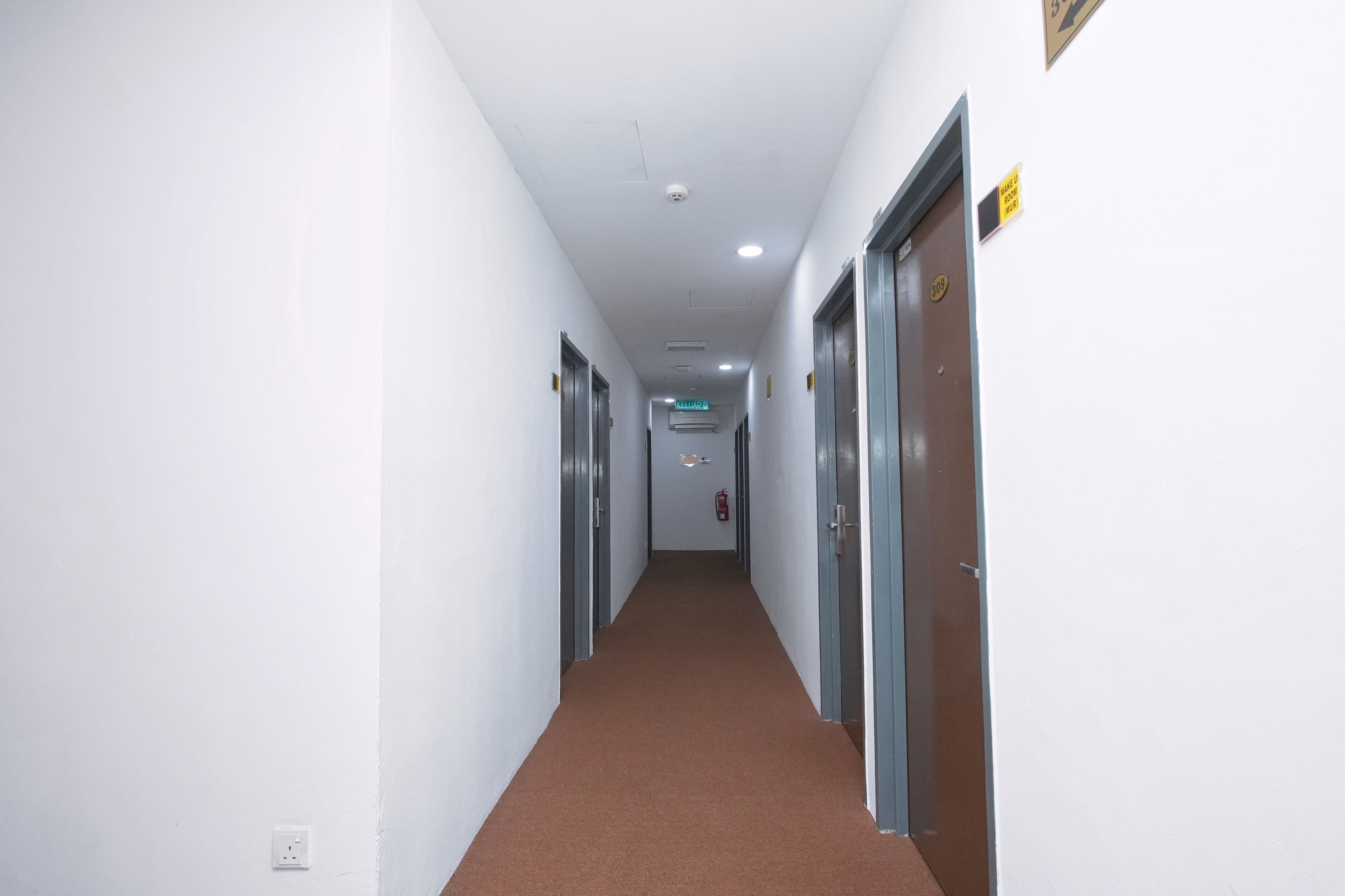 Un couloir aux murs blancs, avec un tapis marron et des portes de part et d’autre.