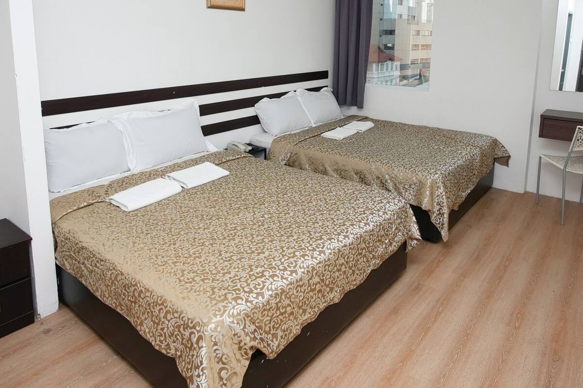 Habitación de hotel con dos camas, un escritorio pequeño, una silla y una ventana con cortinas.