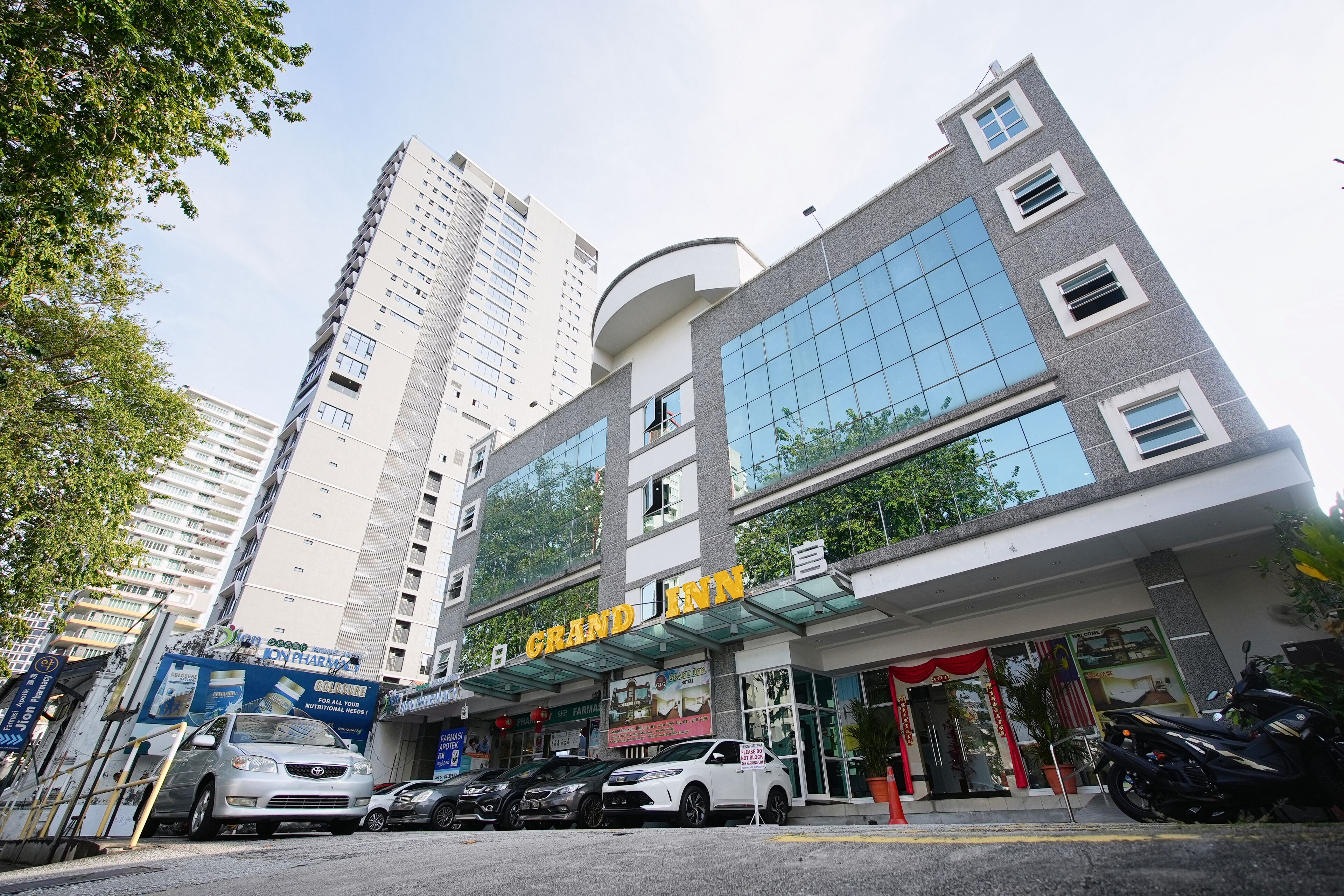 A hotel with a modern facade, a prominent sign, and a parking area with several cars.