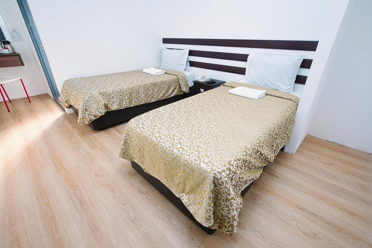 Dos camas individuales con cubrecamas estampados en una habitación con piso de madera y paredes blancas.