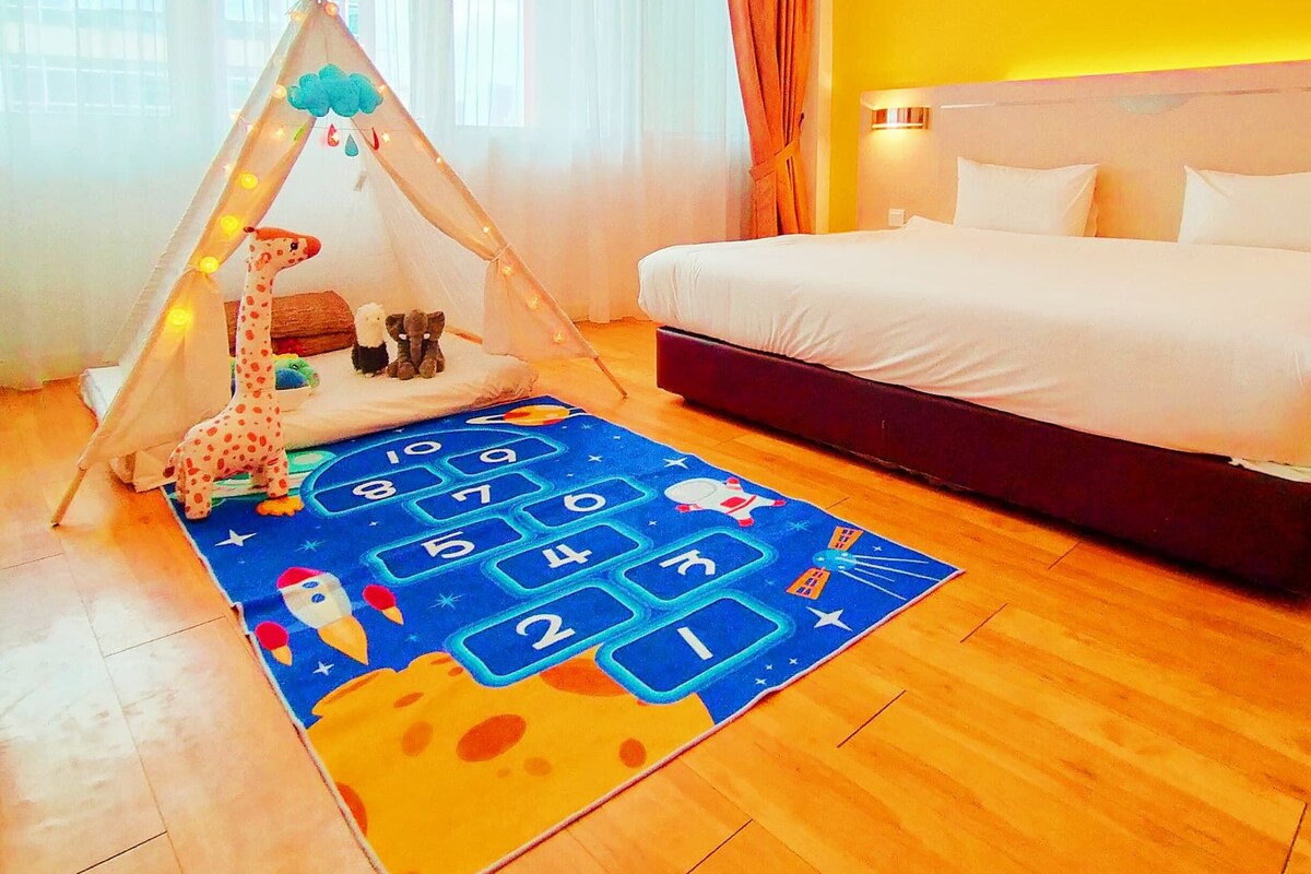 Una habitación de hotel con una cama, una tienda de campaña con juguetes y un tapete de juegos.