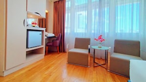 A hotel room with a wooden floor, a small table with a vase, two armchairs, a sofa, a TV, and a mini-fridge. - Sentral Georgetown (George Town)